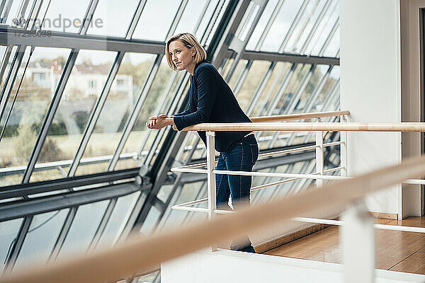 Weibliche Unternehmerin schaut weg  während sie sich auf ein Geländer stützt