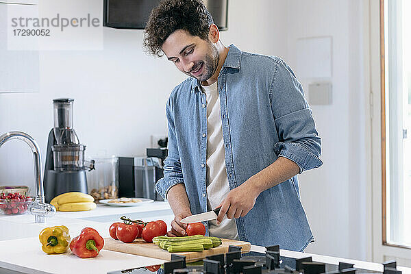 Lächelnder erwachsener Mann  der in der Küche zu Hause Tomaten schneidet