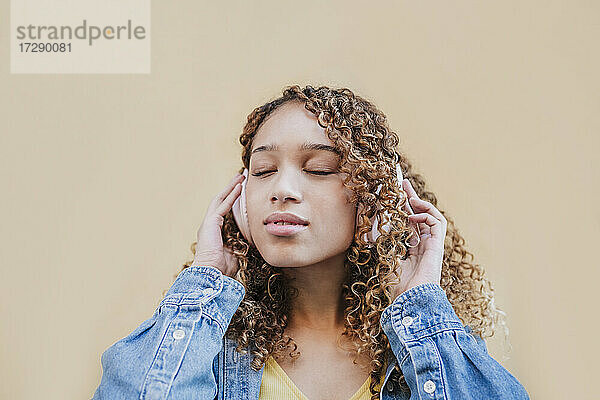 Schöne Frau mit geschlossenen Augen hört Musik auf Kopfhörer durch beige Wand