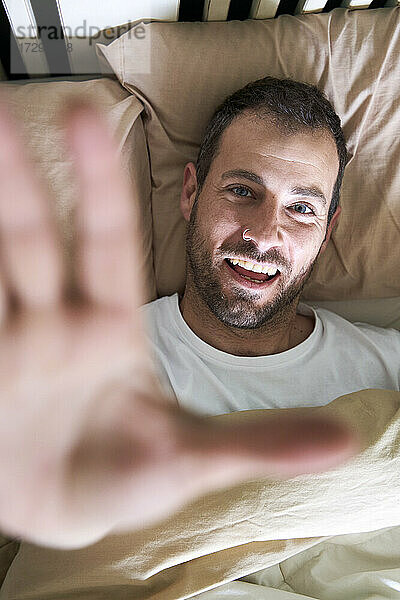 Mann streckt seine Hand aus  während er im Bett liegt