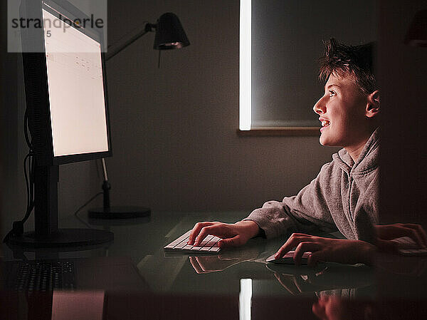 Lächelnder Junge  der einen Computer benutzt  während er zu Hause lernt