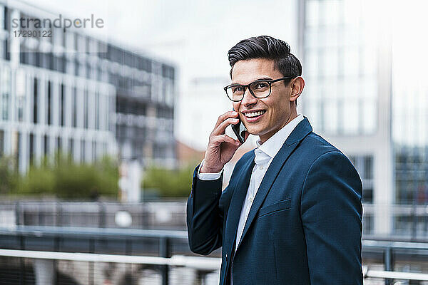 Lächelnder Geschäftsmann  der am Geländer mit einem Mobiltelefon spricht