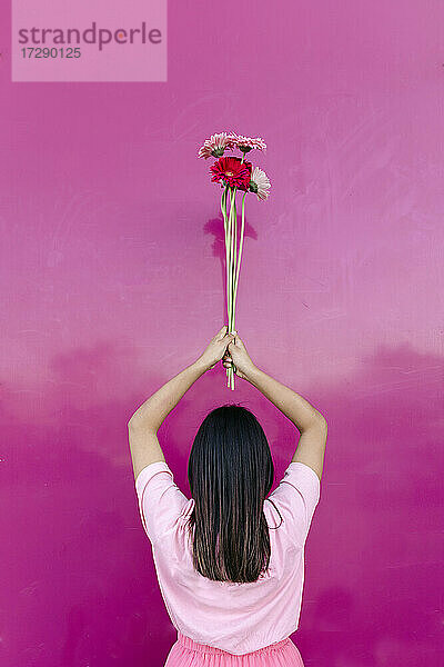 Frau mit erhobenen Armen und Blumen vor einer rosa Wand