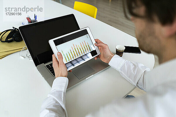 Männlicher Unternehmer  der bei der Arbeit im Büro eine Grafik auf einem digitalen Tablet überprüft