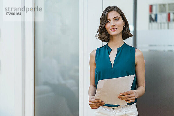 Schöne junge Unternehmerin mit Dokumenten an der Tür im Büro stehend