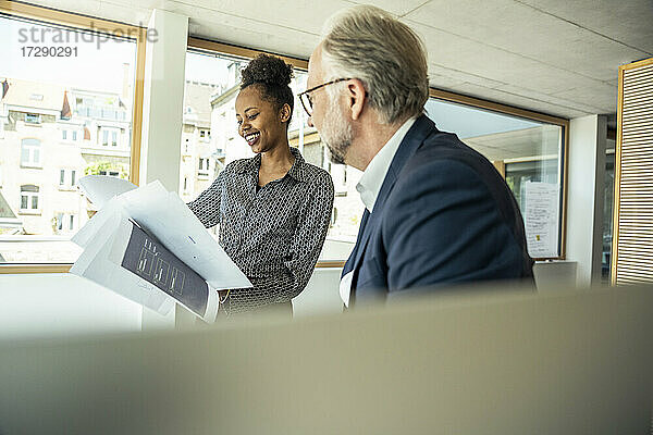 Lächelnde Geschäftsfrau mit einem männlichen Kollegen  der eine Strategie im Büro betrachtet