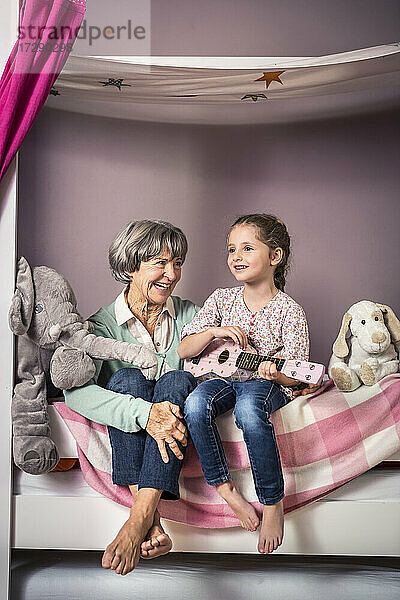 Enkelin spielt Gitarre und sitzt neben der Großmutter auf dem Bett