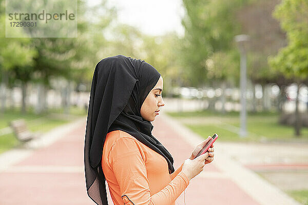 Arabische Frau mit Kopftuch benutzt ein Smartphone in einem öffentlichen Park