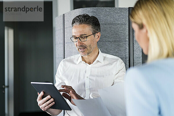Geschäftsmann  der ein digitales Tablet benutzt  während er sich mit einer Mitarbeiterin im Büro unterhält
