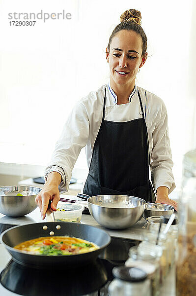 Lächelnde weibliche Köchin beim Kochen von Speisen in einer Pfanne im Restaurant