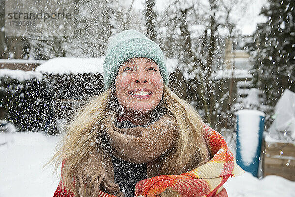 Fröhliche reife Frau mit Strickmütze und Schal bei Schneefall im Winter