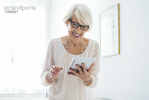 Lächelnde ältere Frau  die zu Hause ein digitales Tablet benutzt