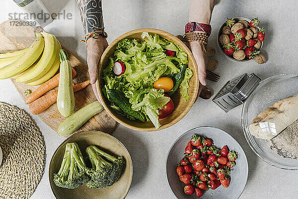 Mann hält Salatschüssel mit Gemüse und Obst auf dem Tisch