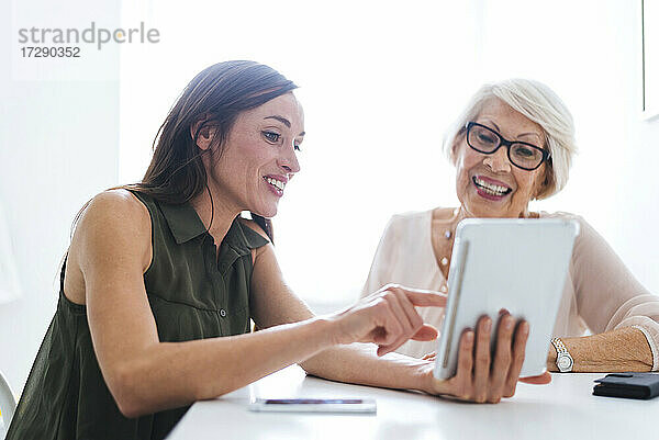 Lächelnde Frau zeigt digitales Tablet im Gespräch mit Großmutter zu Hause