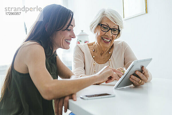 Lächelnde ältere Frau  die ihr digitales Tablet mit ihrer Enkelin zu Hause teilt