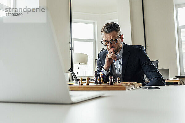 Geschäftsmann schaut auf Laptop beim Schachspielen im Büro