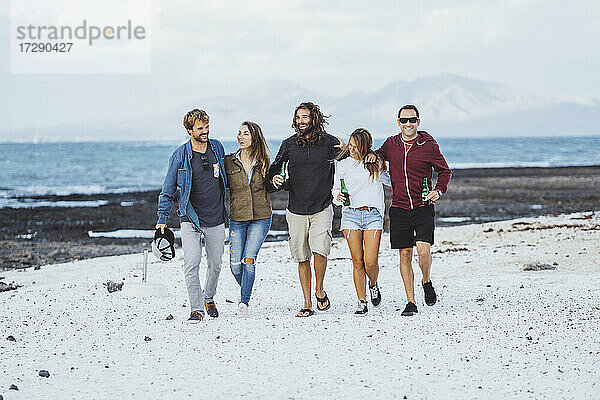 Lächelnde Freunde  die gemeinsam auf dem Sand spazieren gehen