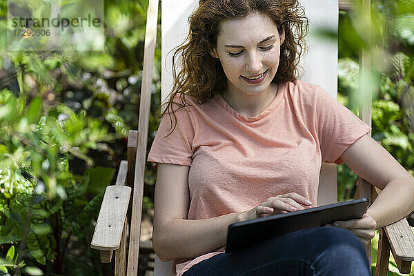 Junge Frau benutzt digitales Tablet auf einem Stuhl im Garten