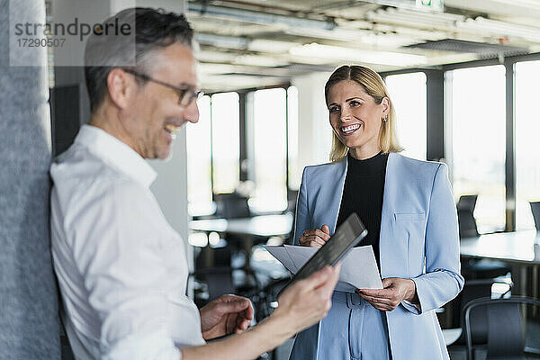 Lächelnde Unternehmerin  die einen männlichen Kollegen bei der Nutzung eines digitalen Tablets im Büro beobachtet