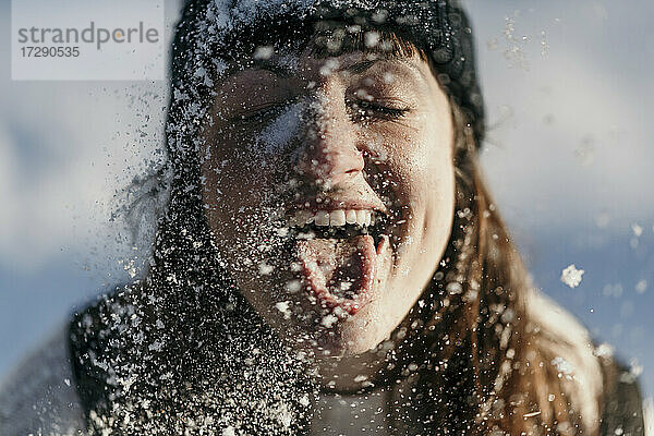 Mittlere erwachsene Frau streckt beim Spielen im Schnee die Zunge heraus