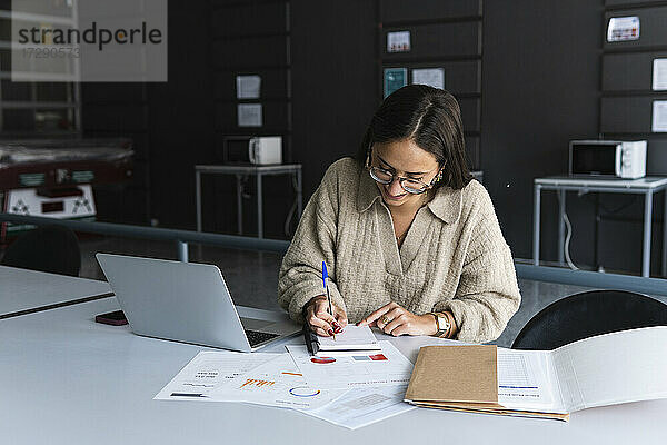 Weibliche Fachkraft mit Brille schreibt im Büro in ein Tagebuch