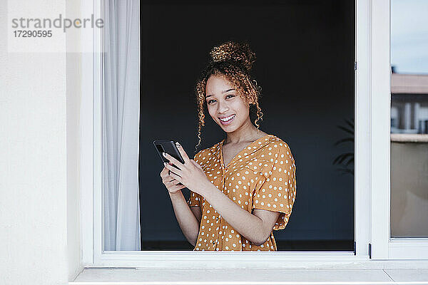 Schöne Frau mit Mobiltelefon am Fenster stehend