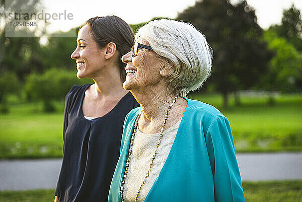 Lächelnde Großmutter schaut weg  während sie bei ihrer Enkelin im Park steht