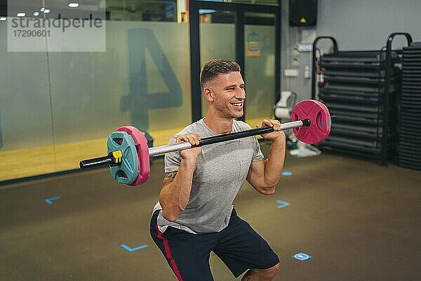 Lächelnder männlicher Sportler beim Training mit einer Langhantel im Fitnessstudio