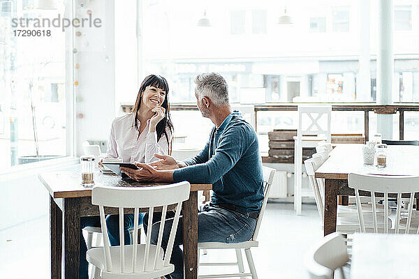 Geschäftsmann mit digitalem Tablet erklärt einem Kollegen  während er in einem Cafe sitzt