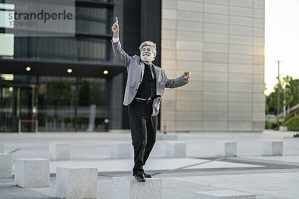 Fröhlicher Geschäftsmann tanzt auf Betonblock bei Bürogebäude