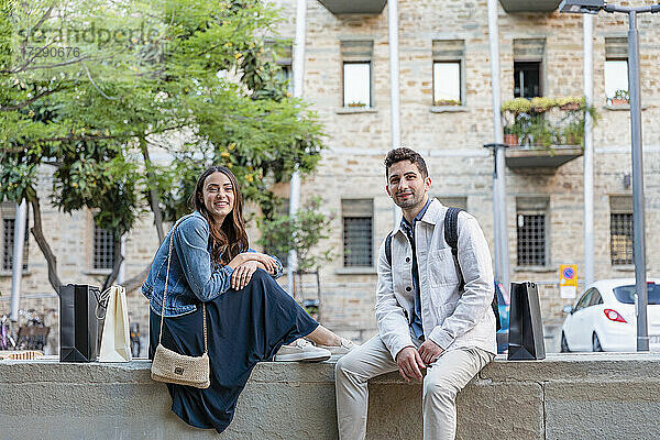 Lächelndes Touristenpaar auf einer Betonstützmauer sitzend