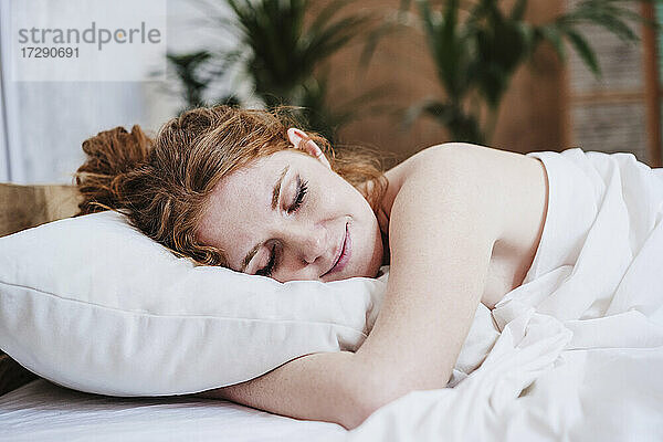 Hemdlose Frau mit Decke auf dem Bett liegend zu Hause