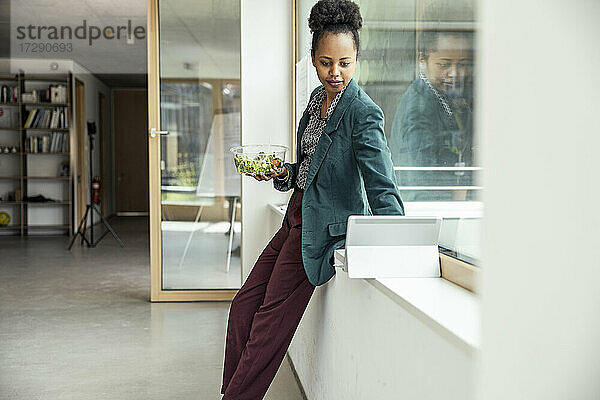 Geschäftsfrau mit Salatschüssel und digitalem Tablet im Büro