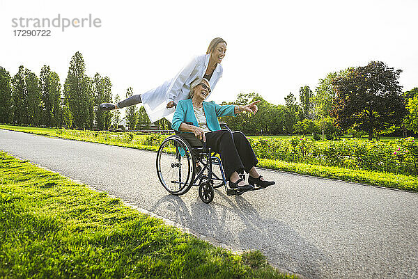 Verspielte Hausmeisterin vergnügt sich mit älterer Frau im Rollstuhl im Park