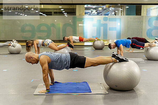 Männliche und weibliche Sportler balancieren im Fitnessstudio auf einem Fitnessball