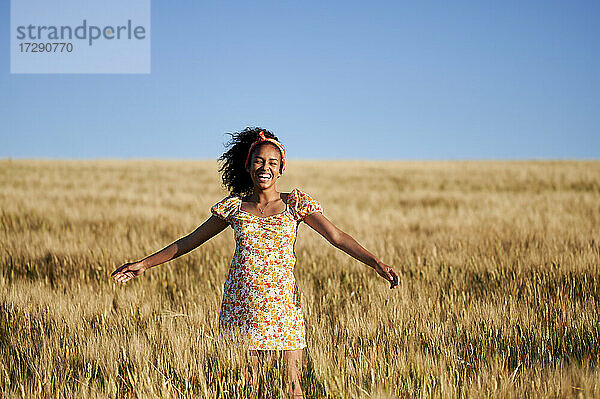 Fröhliche junge Frau mit ausgestreckten Armen in einem Weizenfeld stehend