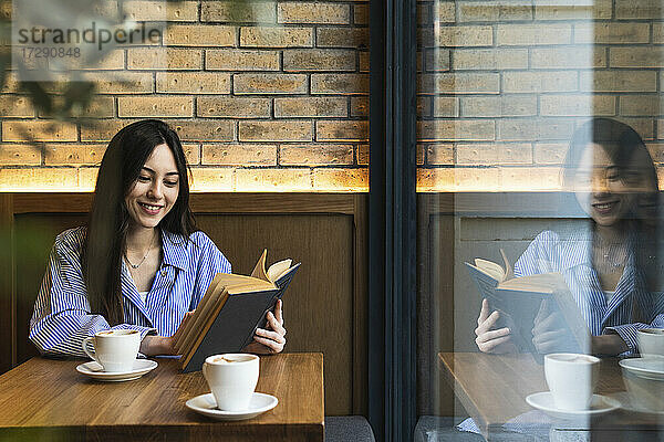 Lächelnde junge Frau  die an einer Bar ein Buch liest