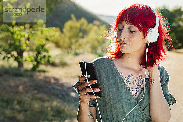 Hipster-Frau mit roten Haaren  die ein Smartphone an einem sonnigen Tag benutzt