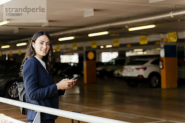 Geschäftsfrau hält Smartphone auf einem Parkplatz