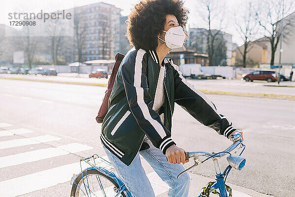 Frau mit Gesichtsmaske  die an einem sonnigen Tag Fahrrad fährt