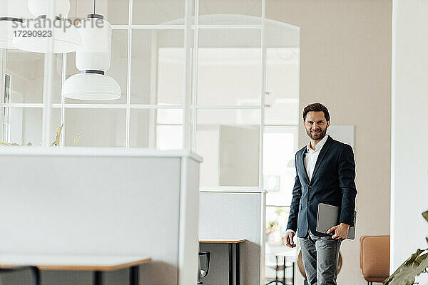 Lächelnder Geschäftsmann  der ein digitales Tablet hält  während er im Büro steht