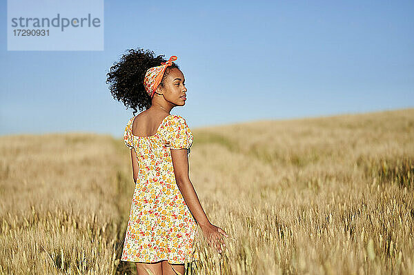 Junge Frau mit lockigem Haar  die in einem Weizenfeld steht und wegschaut