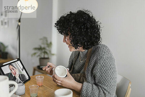 Lächelnde Künstlerin mit Tasse  die in einem Workshop mit einem digitalen Tablet lernt