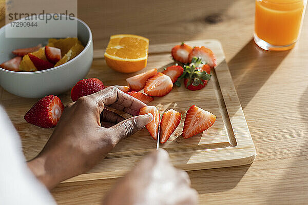Hände einer Frau beim Schneiden frischer Erdbeeren am Küchentisch