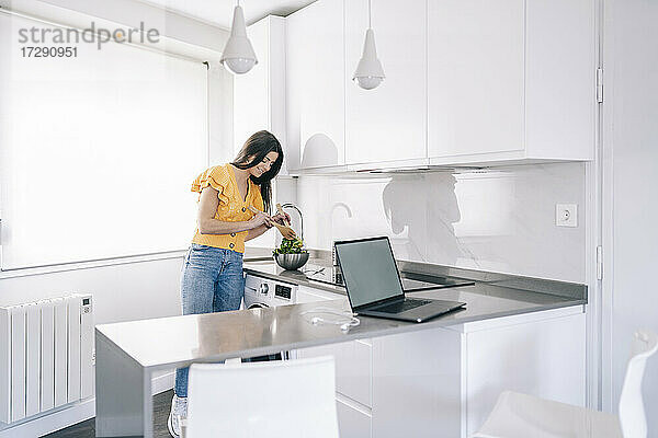 Frau bereitet Salat zu  während sie zu Hause an der Küchentheke steht