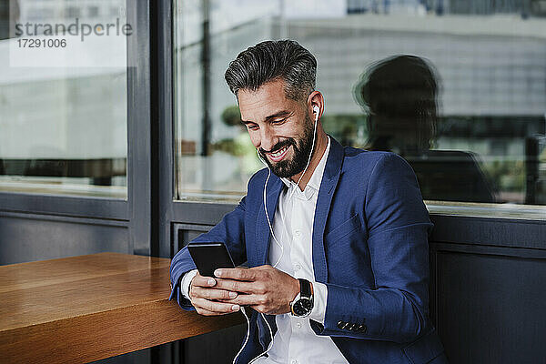 Männlicher Unternehmer  der ein Mobiltelefon benutzt  während er in der Cafeteria sitzt