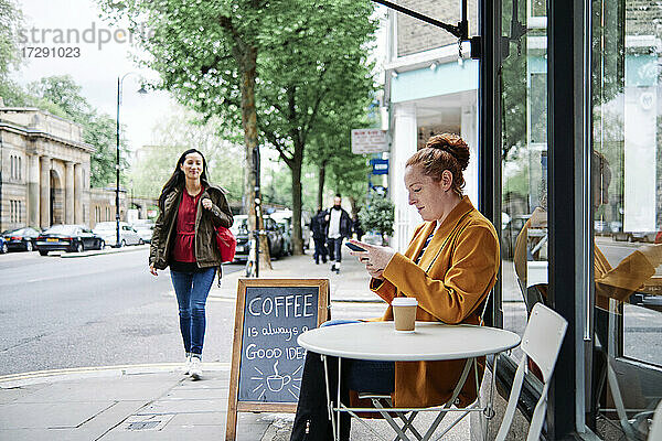 Frau benutzt Mobiltelefon in einem Straßencafé