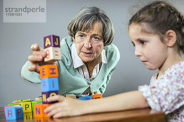 Ältere Frau stapelt Spielzeugblock beim Spielen mit Mädchen zu Hause
