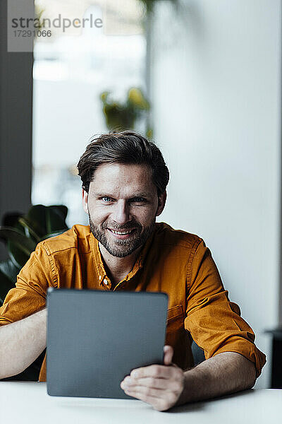 Männlicher Unternehmer mit digitalem Tablet lächelnd im Büro