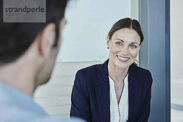 Lächelnde Geschäftsfrau  die einen Mann ansieht  während sie mit ihm diskutiert